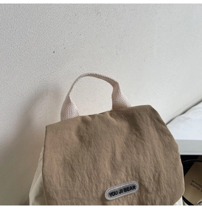 Close-up of minimalist nylon backpack showing brown flap, woven handle and logo tag detail
