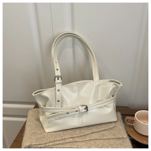 Detail of creamy white patent leather tote bag with silver buckle on knitted blanket