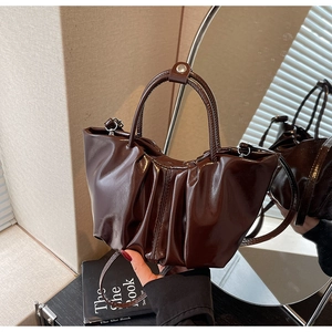 Detailaufnahme der plissierten dunkelbraunen Handtasche mit Hochglanzfinish und Ringgriff