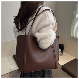 Deep brown leather tote bag worn on shoulder in a warm minimalist indoor setting