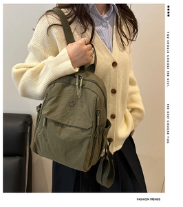 Close-up of olive green nylon backpack with front zipper pocket and metal logo detail
