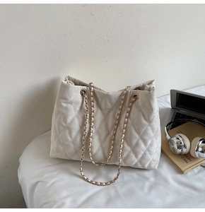 Gros plan sur un sac cabas matelassé crème avec chaîne dorée et accessoires chic