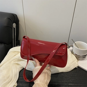 Close-up of hand holding a glossy red patent leather baguette bag with a sleek flap design