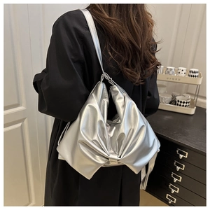 Detailed view of metallic silver bow-shaped tote bag worn over the shoulder by a model