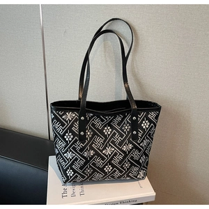 Detail of black tote bag featuring silver geometric patterns and leather shoulder straps