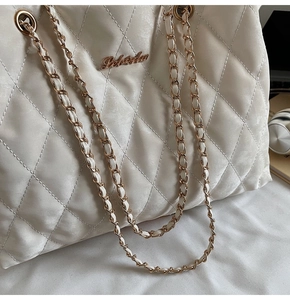 Gros plan sur la texture matelassée beige et la chaîne en métal doré d'un sac à main