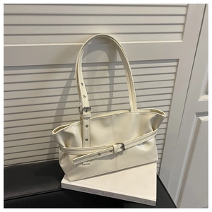 Close-up of cream patent leather tote with decorative buckle and dual shoulder straps