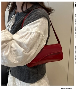Side view of red patent leather underarm bag showing glossy finish and curved flap
