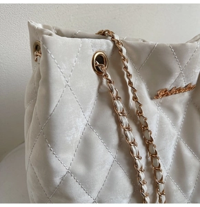 Détail macro du motif matelassé beige et du logo en métal doré sur le sac à main