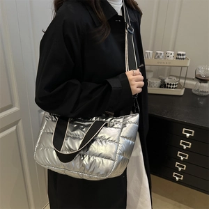 Silver metallic quilted puffer tote bag with striped straps worn by model in minimalist room