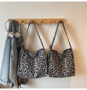 Detail of leopard print canvas tote bags in white and grey hanging on a wooden rack