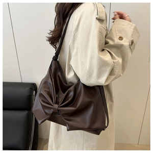 Detail of a large brown shoulder bag with a stylish pleated bow design in soft leather
