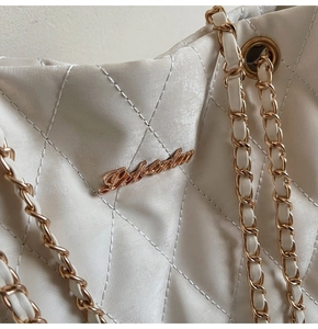 Gros plan sur le matelassage et le logo doré du sac bandoulière blanc à chaîne