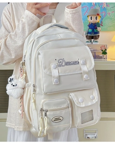 Detail of a beige multi-pocket student backpack with a cute bear plush keychain charm