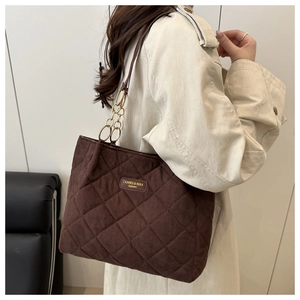Detail of brown quilted corduroy tote bag showing gold chain link and leather brand tag