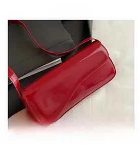 Detail of red patent leather shoulder bag with glossy finish and curved flap closure