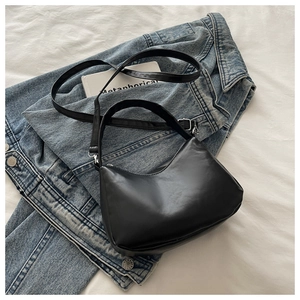 Détail d'un sac demi-lune noir avec nœud sur un fond en jean décontracté