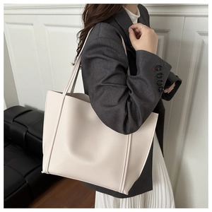 Detailed view of a cream-colored leather tote bag worn by a model in a minimalist setting