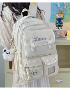 Detail of cream white nylon backpack featuring multiple functional pockets and cute bear charm