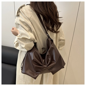 Detailed side view of deep brown oversized bow shoulder bag on a beige trench coat