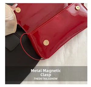 Detail of red patent leather shoulder bag with gold magnetic snaps and glossy finish