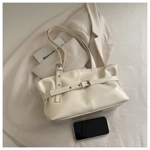 Close-up of cream patent leather tote with adjustable buckle and minimalist strap details