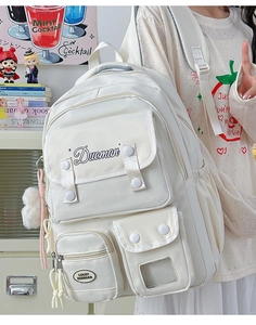 Detail of cream backpack with multiple functional pockets and a plush pompom pendant