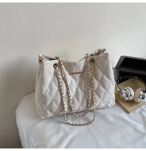 Gros plan du sac cabas matelassé beige avec chaînes dorées et logo métallique
