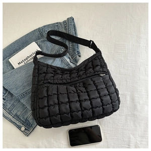Detailed view of black quilted puff shoulder bag with adjustable strap on denim jacket