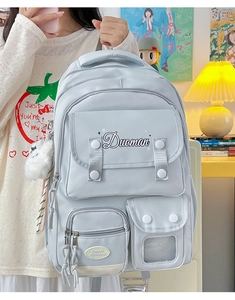 Close-up of light blue multi-pocket school backpack with a plush ball charm detail