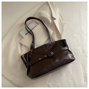 Detail of a dark brown patent leather tote bag with belt buckle and slim shoulder straps