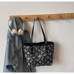 Detail of black tote bag with white geometric embroidery and silver metal rivets