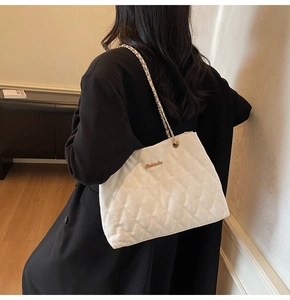 Détail d'un sac cabas blanc matelassé avec bandoulière en chaîne dorée porté par un modèle