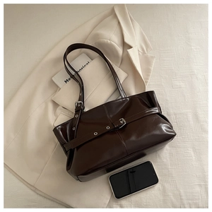 Macro shot of dark brown glossy leather tote bag with stylish decorative belt and metal buckle