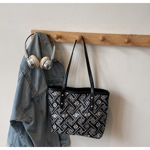 Detail of black tote bag with silver geometric embroidery and leather handles on rack