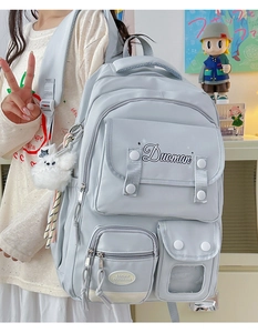 Detail of light blue waterproof nylon backpack with multiple pockets and white bear charm