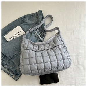 Macro shot of light blue quilted puff bag featuring a zip pocket and adjustable strap