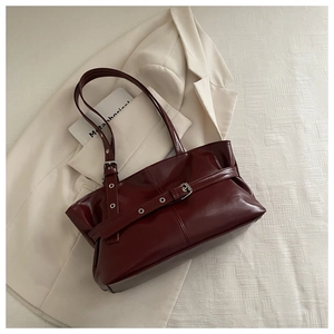 Macro detail of glossy burgundy tote bag featuring stylish belt buckle and eyelet design