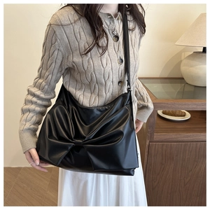 Detail of a black hobo bag with a large bow design and matte leather on a female model