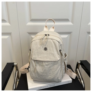 Macro detail of cream nylon backpack featuring a vintage metal logo and textured fabric