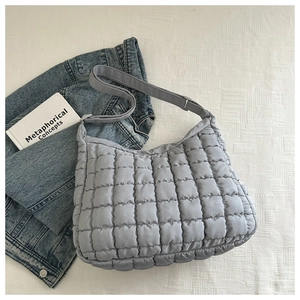 Detail of grey-blue quilted puffer cloud bag with wide strap on minimalist background