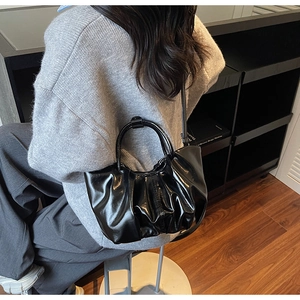 Detailed view of black pleated handbag with high-gloss finish and circular handle