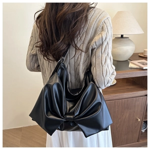 Detail of a black bow-shaped shoulder bag in glossy faux leather with pleated texture