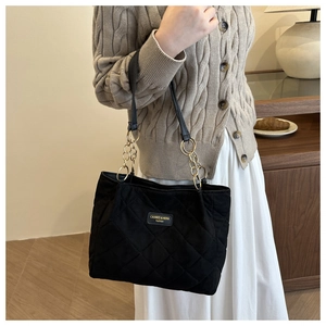Detail of black quilted tote bag with gold chain strap styled on a neutral knit outfit
