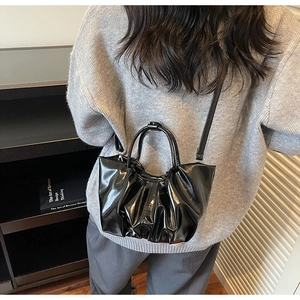 Detail of black pleated cloud tote bag featuring glossy patent leather and shoulder strap