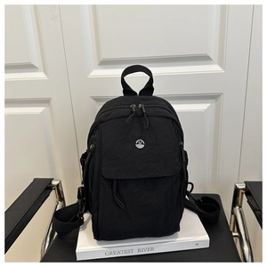 Detail of black oxford fabric backpack featuring metal M logo and multiple pockets