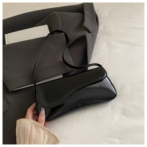 Detail of the glossy black patent leather shoulder bag with a curved flap design