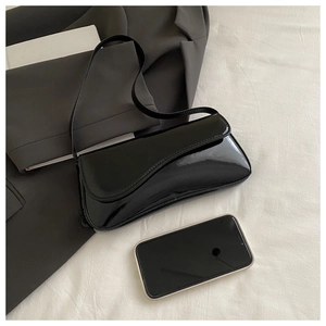 Close-up of black patent leather underarm bag with glossy finish next to a smartphone