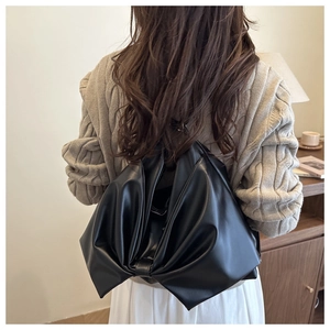 Macro shot of stylish black PU leather bow backpack on model in a cozy interior