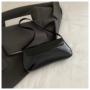 Detailed close-up of glossy black patent leather baguette bag on aesthetic office wear